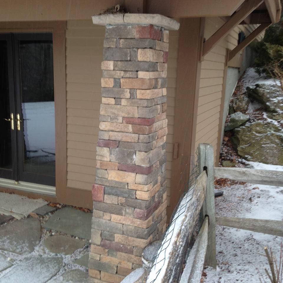 Stone pillar supporting a brown structure next to a fence and snowy ground.