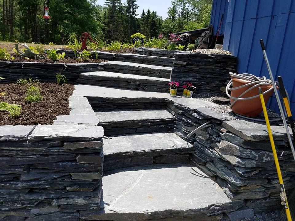 Stone steps leading up to a blue building, with a garden bed and tools visible.