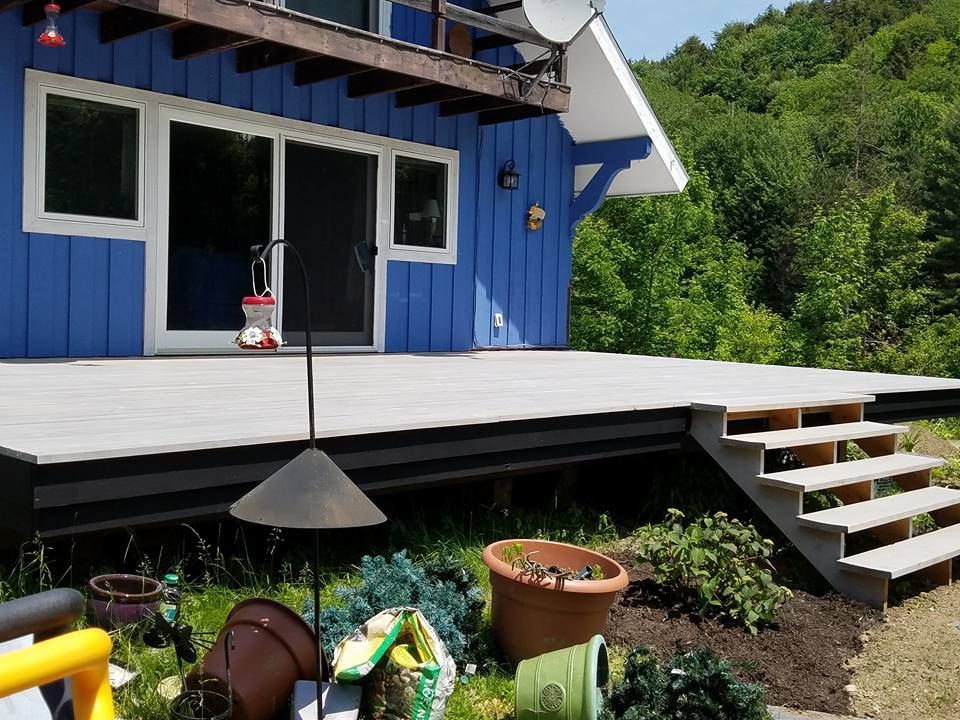 Blue house with gray deck, steps, and greenery. Sliding glass door and hanging bird feeder are visible.