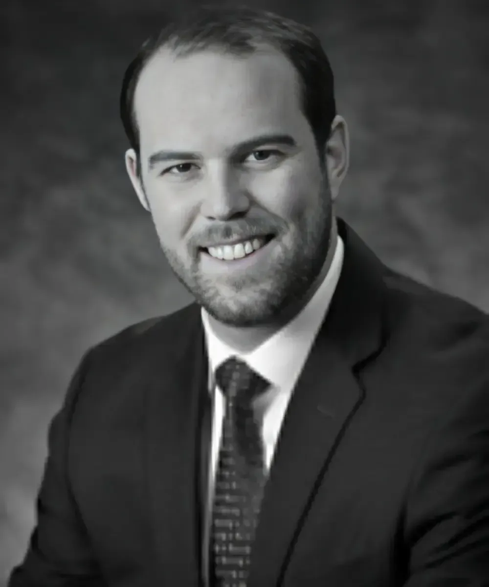 Man in suit smiling, with beard, headshot.
