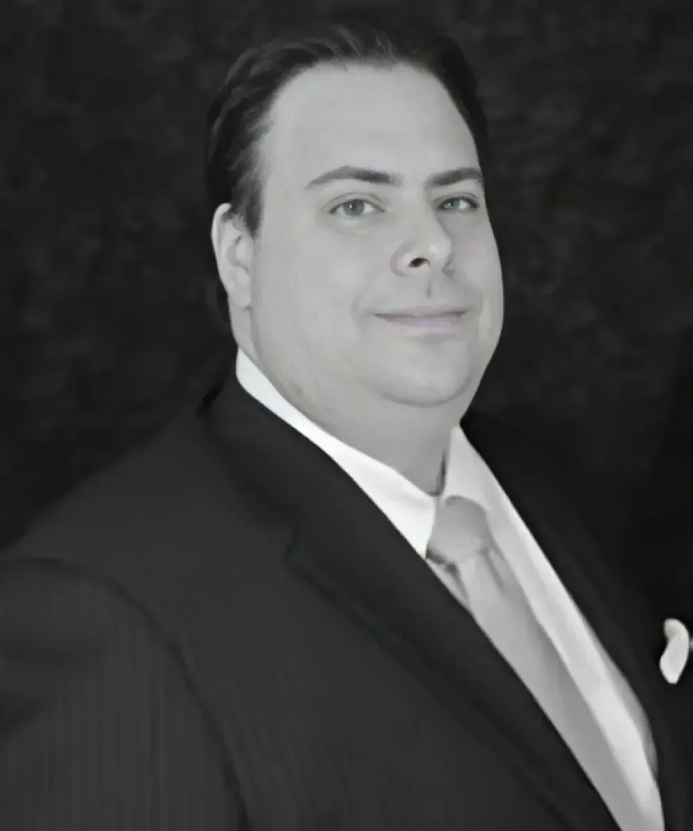 Man in a suit smiles, dark background.