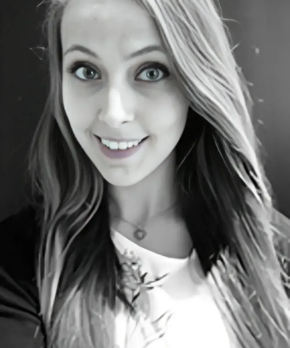 Woman with long, wavy hair, smiling and looking at the camera. She wears a white shirt and a black jacket.