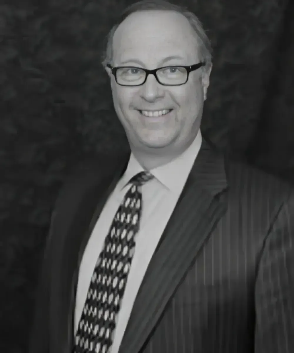 Man in suit and glasses smiling, black and white.