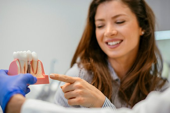 dentist holding dental implant model and woman smiling