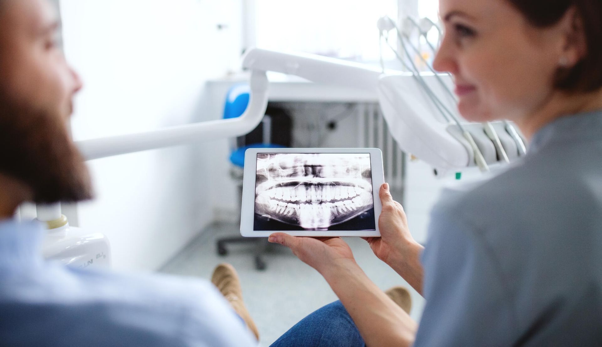 A woman is holding a tablet with a picture of a man 's teeth on it.