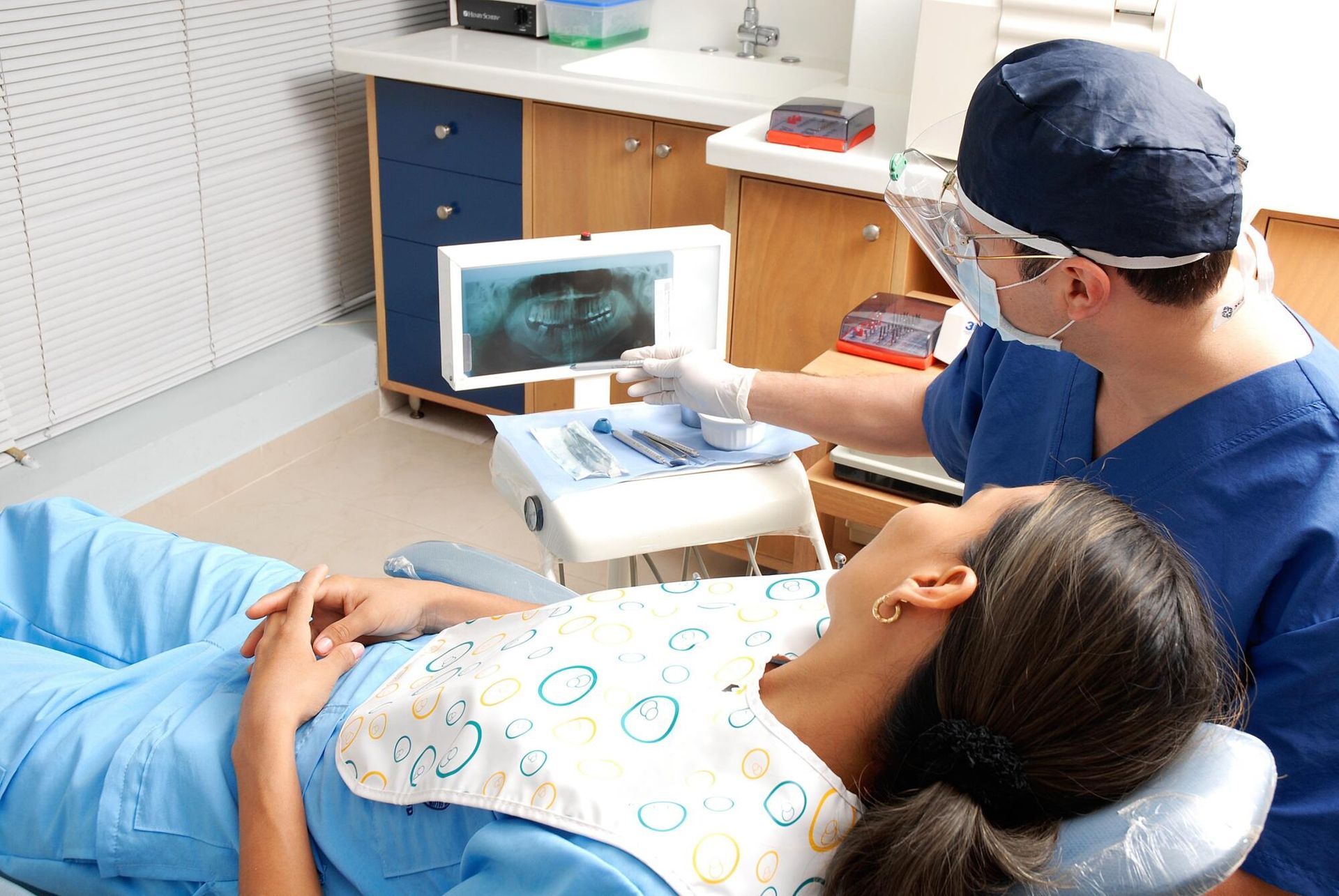 A woman is laying in a dental chair while a dentist examines her teeth