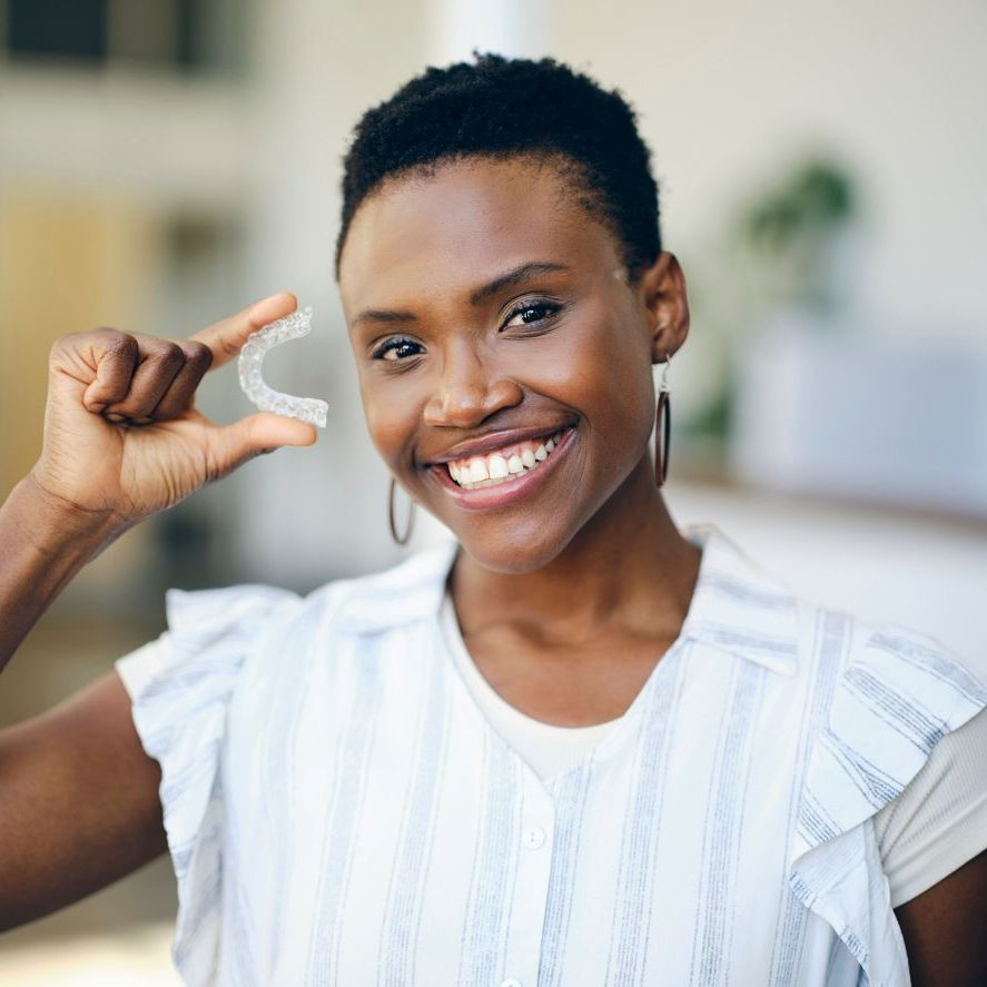 A woman is smiling while holding a clear retainer in her hand.