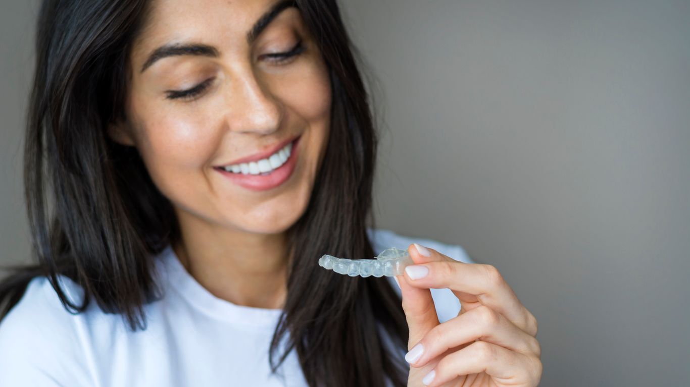 A woman is smiling while holding a clear brace in her hand.