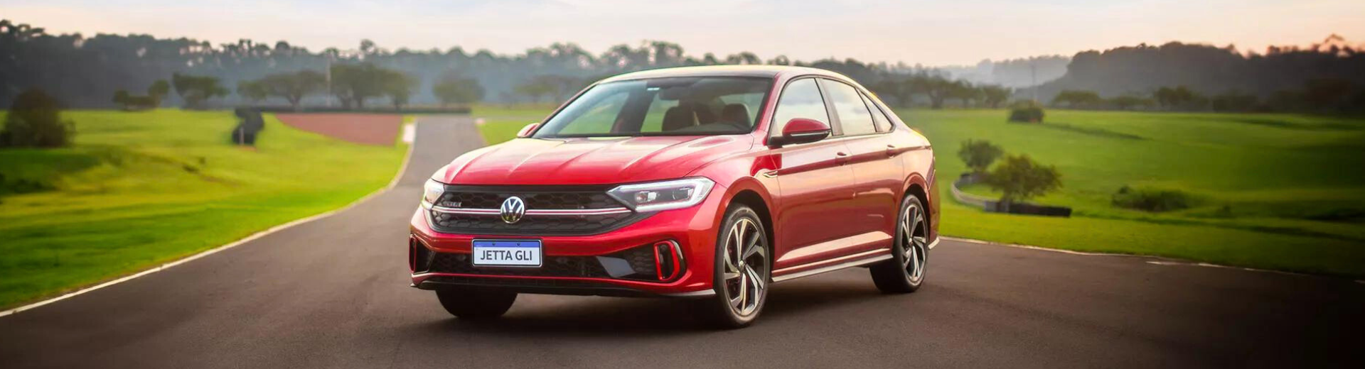 Um volkswagen jetta vermelho está dirigindo em uma estrada rural.