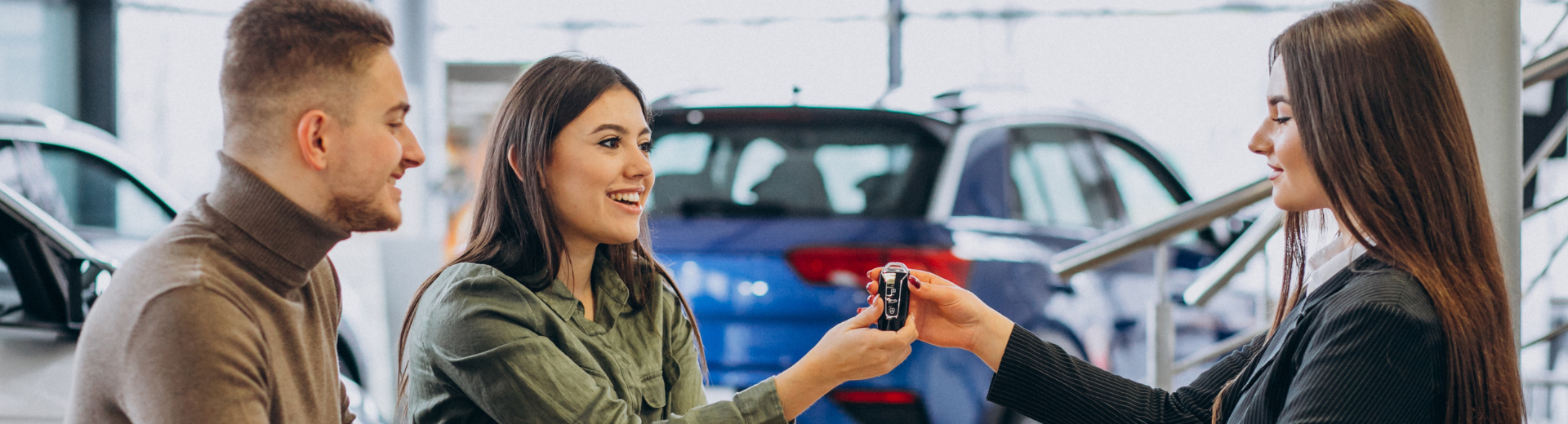 Uma mulher está dando uma chave de carro para um homem e uma mulher em uma concessionária de carros.