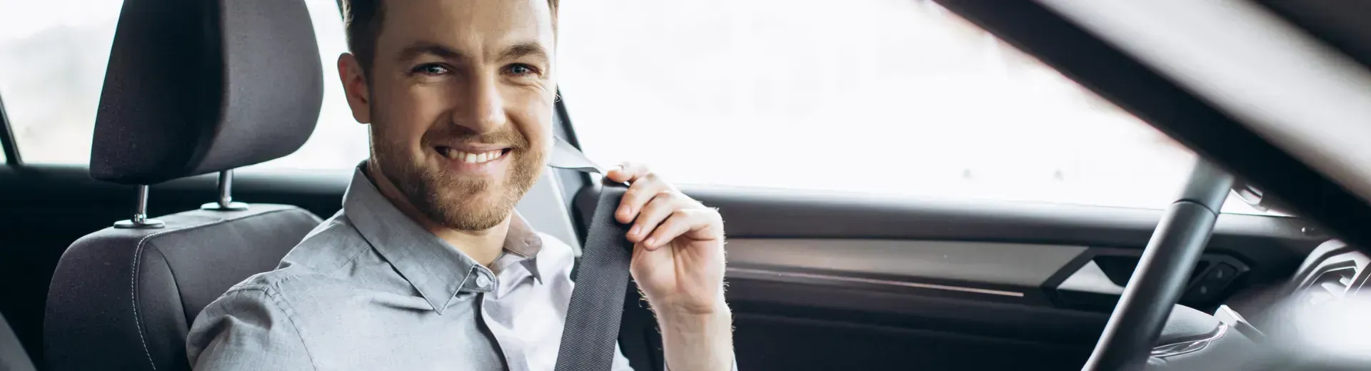 Homem sorrindo dentro de um carro, colocando o cinto de segurança.
