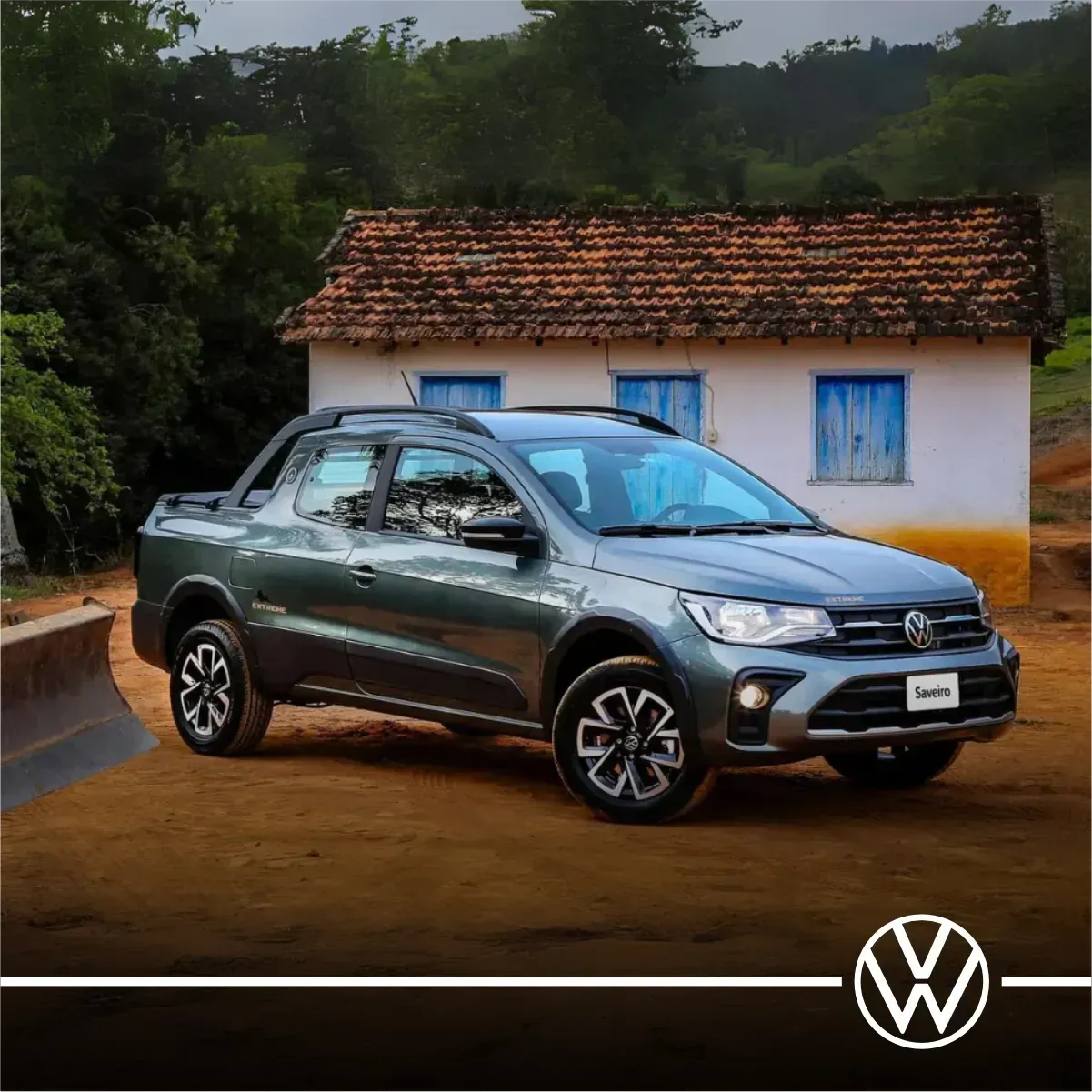 Caminhonete Volkswagen Saveiro cinza estacionada em uma estrada de terra em frente a uma casa branca.