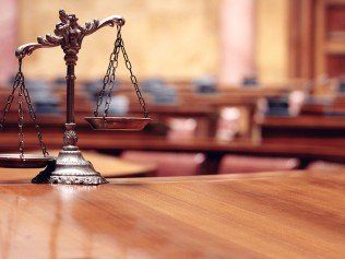 A scale of justice is sitting on a wooden table in a courtroom.