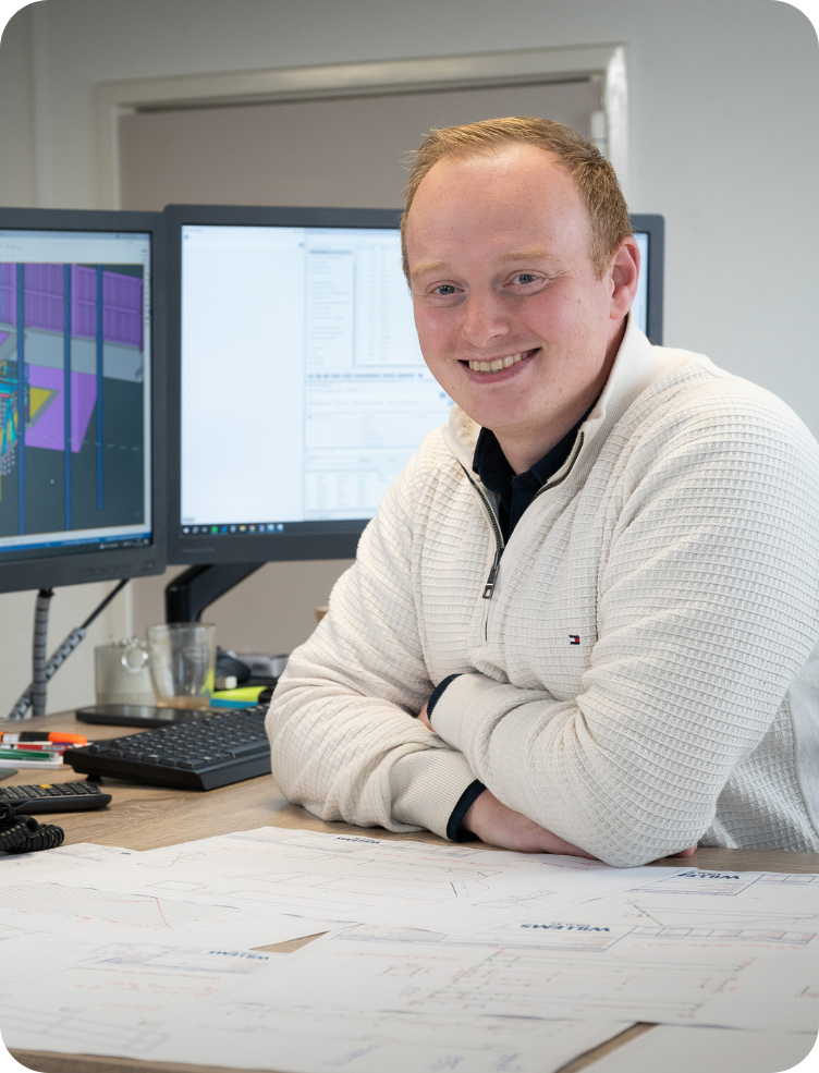 Een man in een blauw shirt staat voor twee computermonitoren. Harm van Ooijen.