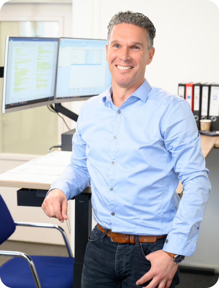 Een man in een blauw shirt staat voor twee computermonitoren. Harm van Ooijen.