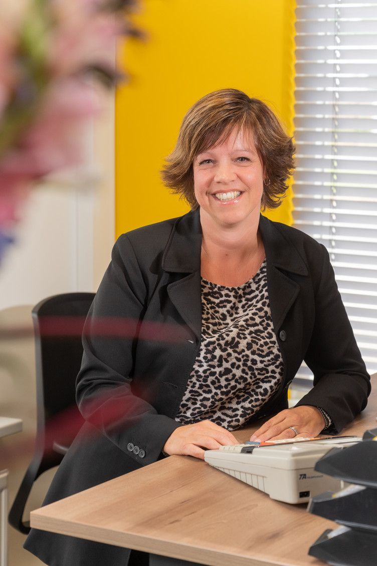 Een vrouw zit aan een bureau met een typemachine en glimlacht.