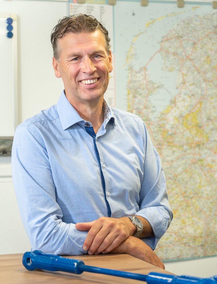 Een man in een blauw shirt zit met zijn armen over elkaar aan een tafel. Marcel Hol. 