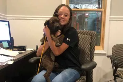 A girl is sitting in an office chair holding a puppy.