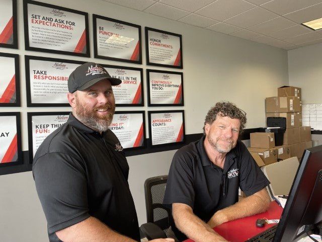 Two men are standing next to each other in front of a wall with plaques that say get and ace for expectations