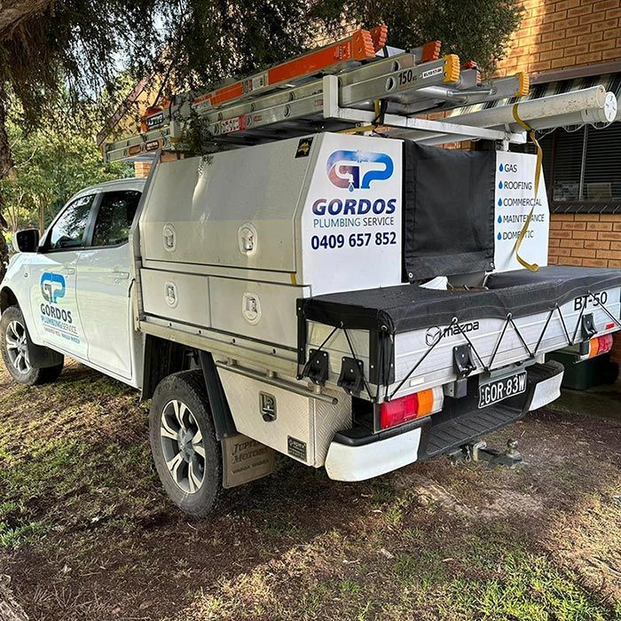 A White Truck with a Ladder on top of it is Parked in Front of a Building — Gordo's Plumbing Service In Wagga Wagga, NSW