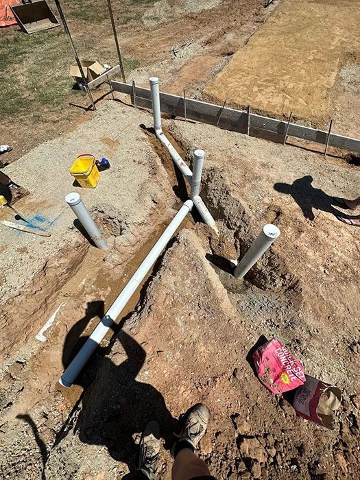 A Person Is Standing In The Dirt Next To A Pile Of Pipes — Gordo's Plumbing Service In Wagga Wagga, NSW