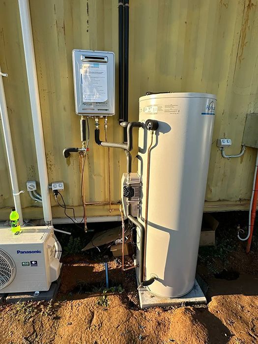 A White Water Heater Is Sitting Next To A Yellow Building — Gordo's Plumbing Service In Wagga Wagga, NSW