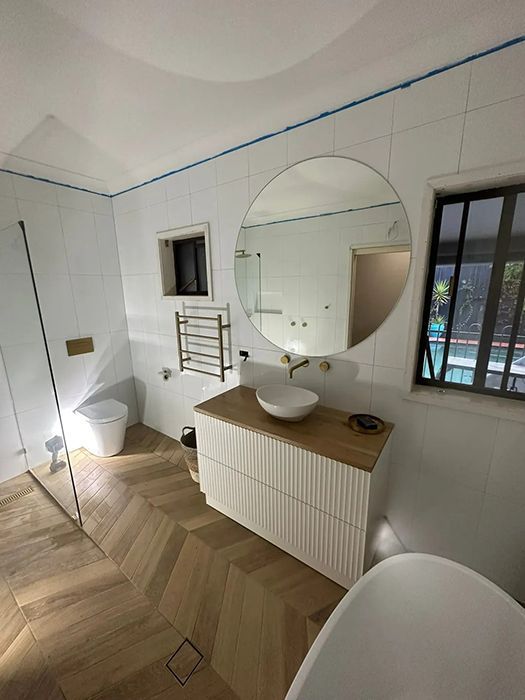 A Bathroom With A Round Mirror, Sink, Toilet And Bathtub — Gordo's Plumbing Service In Wagga Wagga, NSW