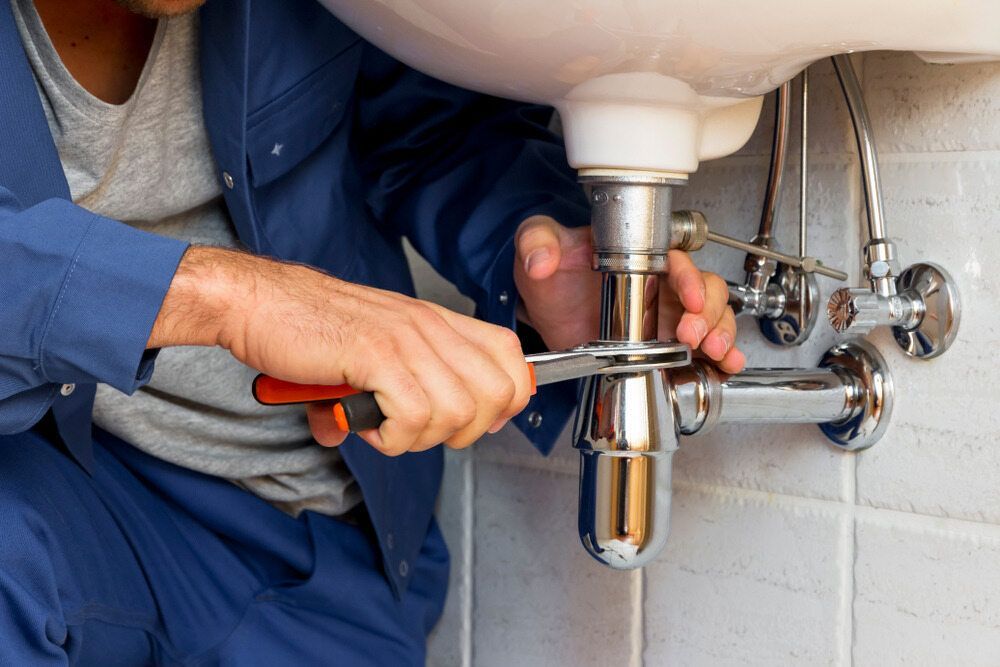 A Plumber Is Fixing A Sink With A Wrench — Gordo's Plumbing Service In Wagga Wagga, NSW