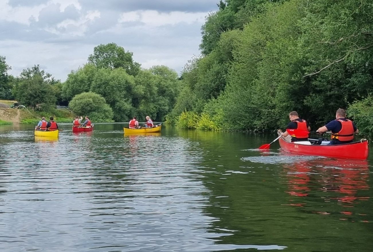 Image of four canoes floating on the River Severn - two red and two yellow. Each canoe contains two people wearing life jackets. 