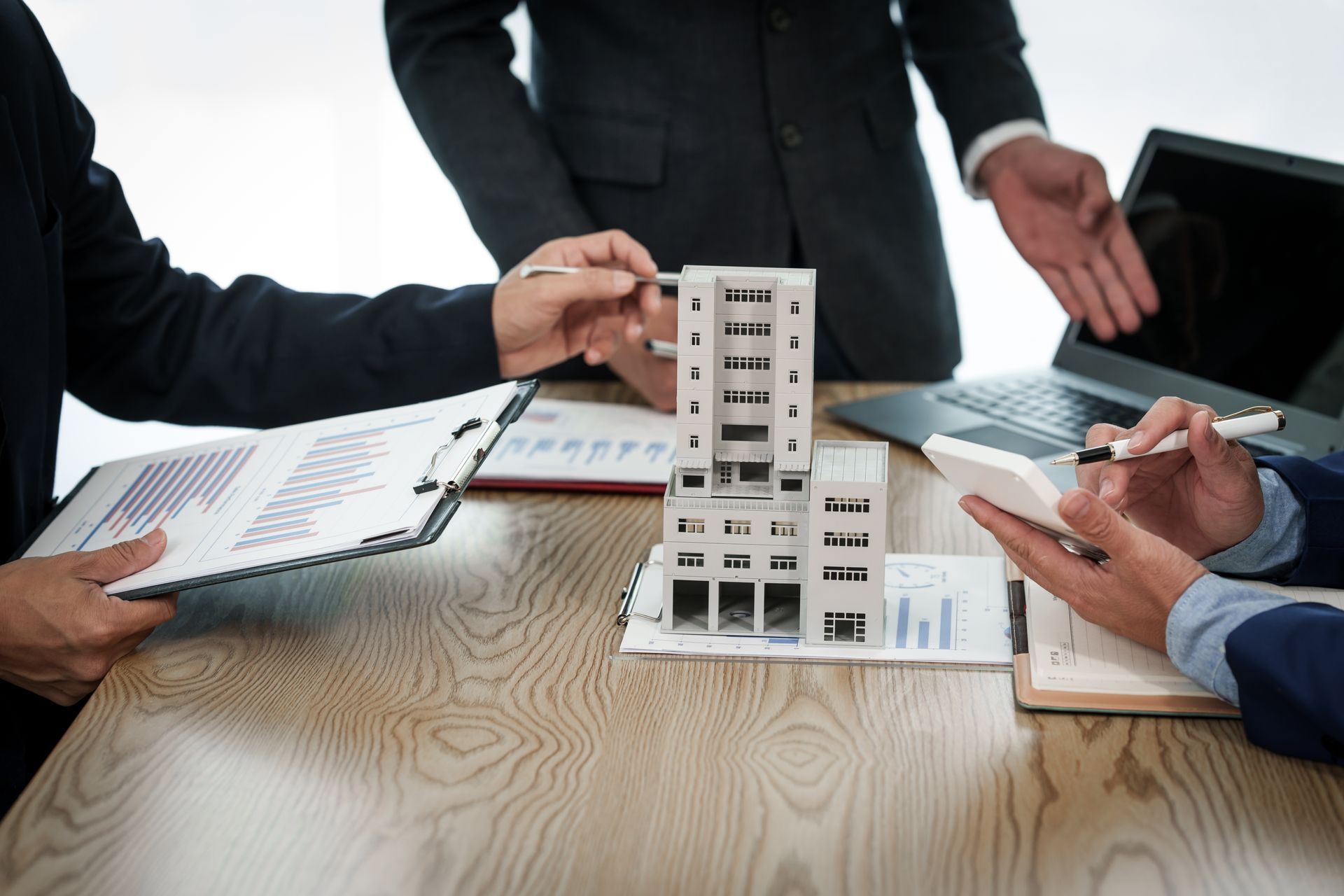 Three professionals in business attire discussing a building model placed on a table over documents.