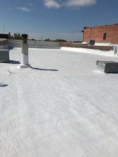 A wide-angle view of a flat, white-coated commercial roof under a clear blue sky, with two HVAC units and a vent pipe.