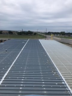 A view looking down a long, metal roof featuring alternating light and dark grey sections against a cloudy sky.