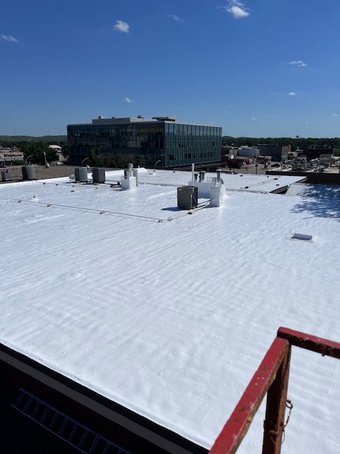 A close-up of a house exterior with dark gray siding, tan shingled gabled roofs, white trim, and a decorative window.
