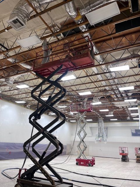 Three red scissor lifts stand in a large, open indoor space with exposed industrial ceiling ductwork.