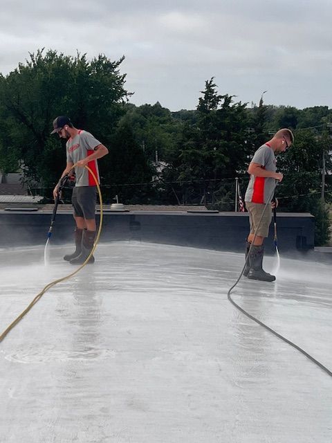 Light gray, multi-story house with brown shingled roofs and white trim under a clear blue sky.