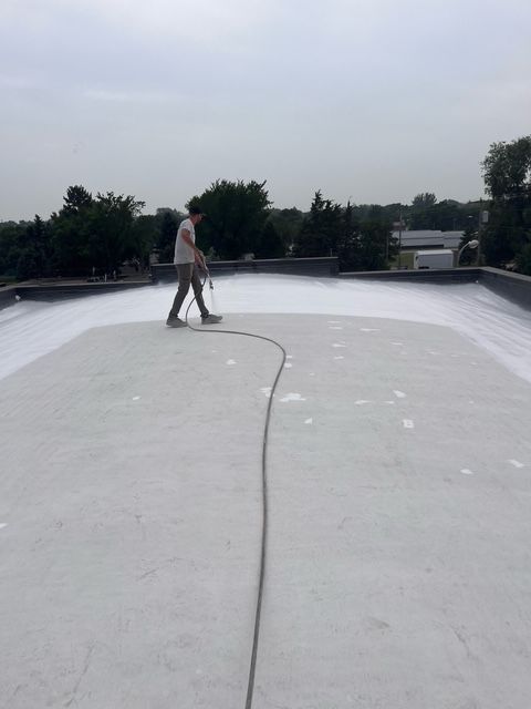 A low-angle view of a brown brick house featuring two gabled roofs with dark brown metal tiling and a gutter system.