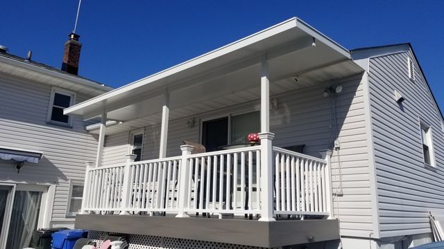 A white house with a white porch and a blue sky in the background - Freehold, NJ - Awning Design Inc