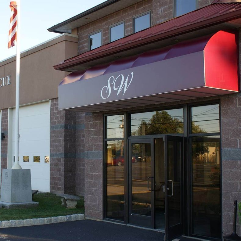 A brick building with a red awning that says sqw - Freehold, NJ - Awning Design Inc