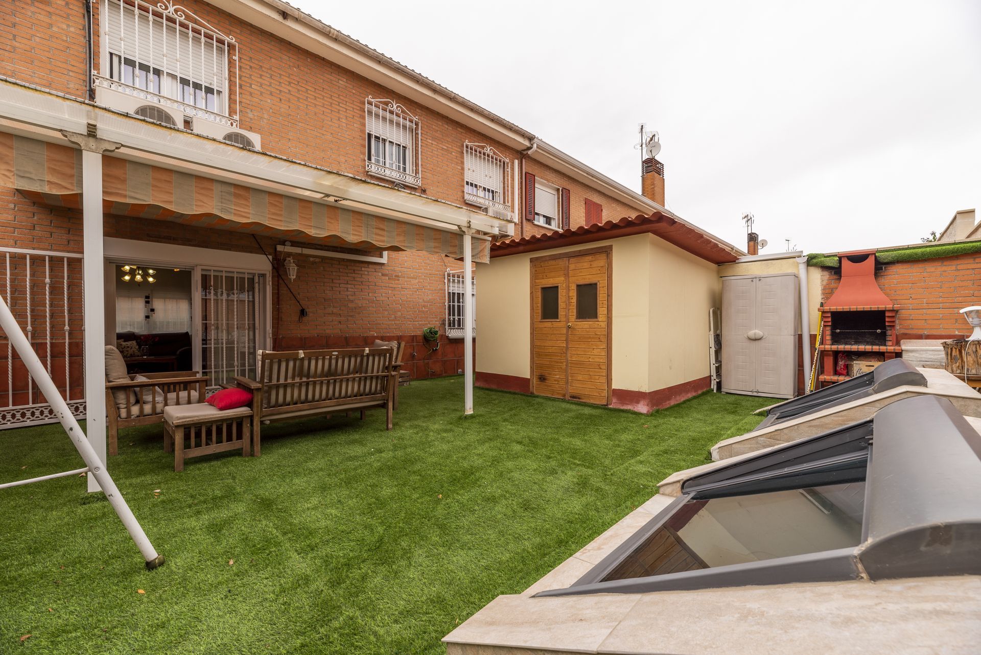 Yellow café exterior with yellow awning, white outdoor tables, chairs, and flower bed. Backyard patio with grass, covered seating, a small shed, and a glass-covered pool or skylight