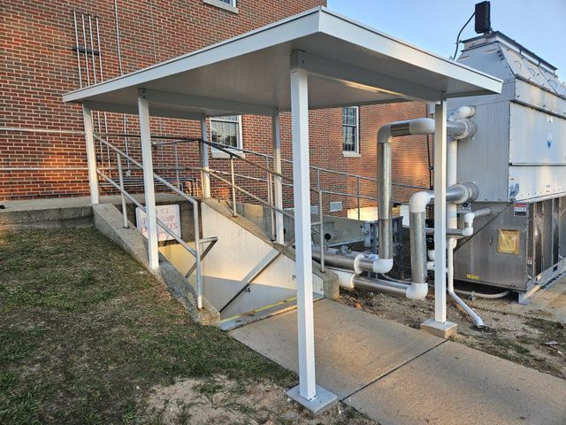 A covered walkway leading to a building with pipes and stairs - Freehold, NJ - Awning Design Inc