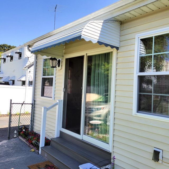 A white house with a blue awning over the front door - Freehold, NJ - Awning Design Inc