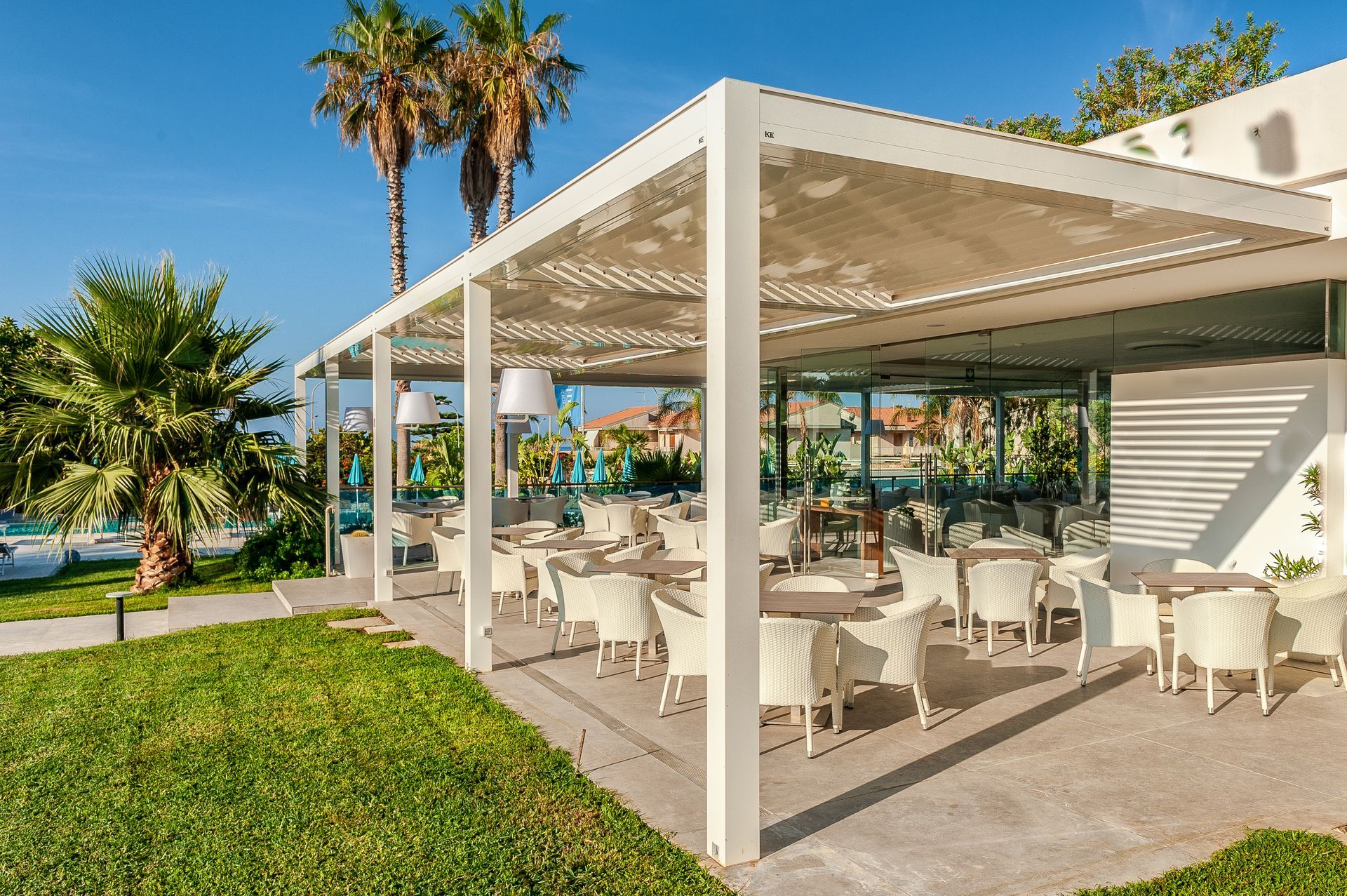 A restaurant with tables and chairs under a pergola with palm trees in the background - Freehold, NJ - Awning Design Inc