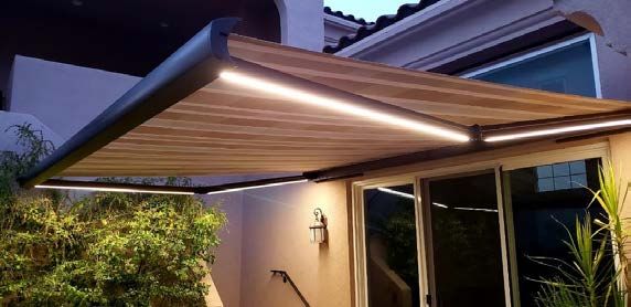 A wooden awning is sitting on top of a patio next to a house - Freehold, NJ - Awning Design Inc
