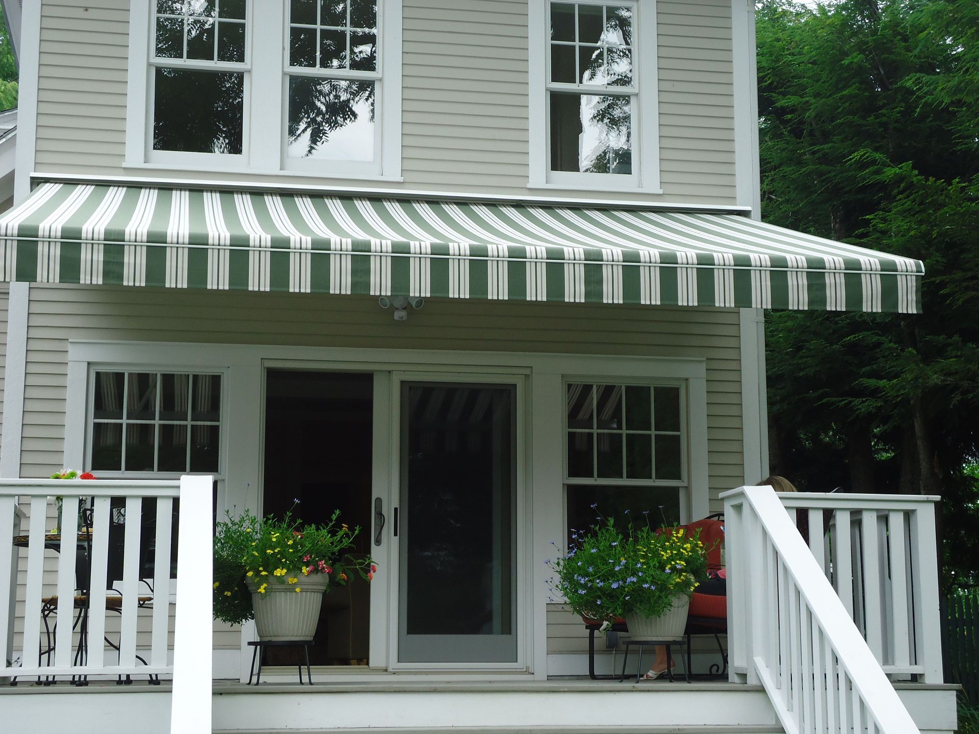 A house with a green and white striped awning over the porch - Freehold, NJ - Awning Design Inc