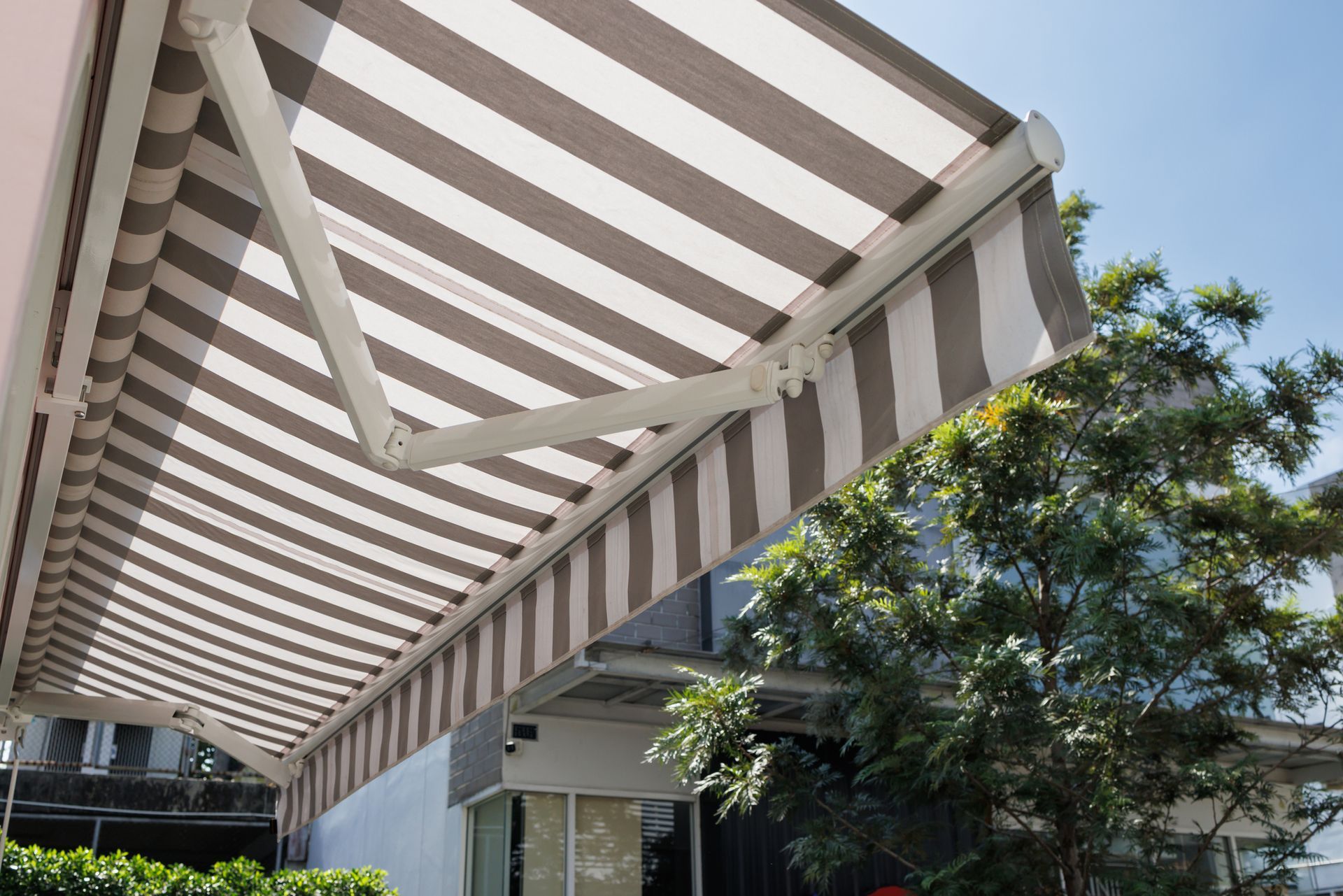 Close-up of a white and gray striped residential awning on a house, and a tree background. Close-up of a white and gray striped residential awning on a house, and a tree background.