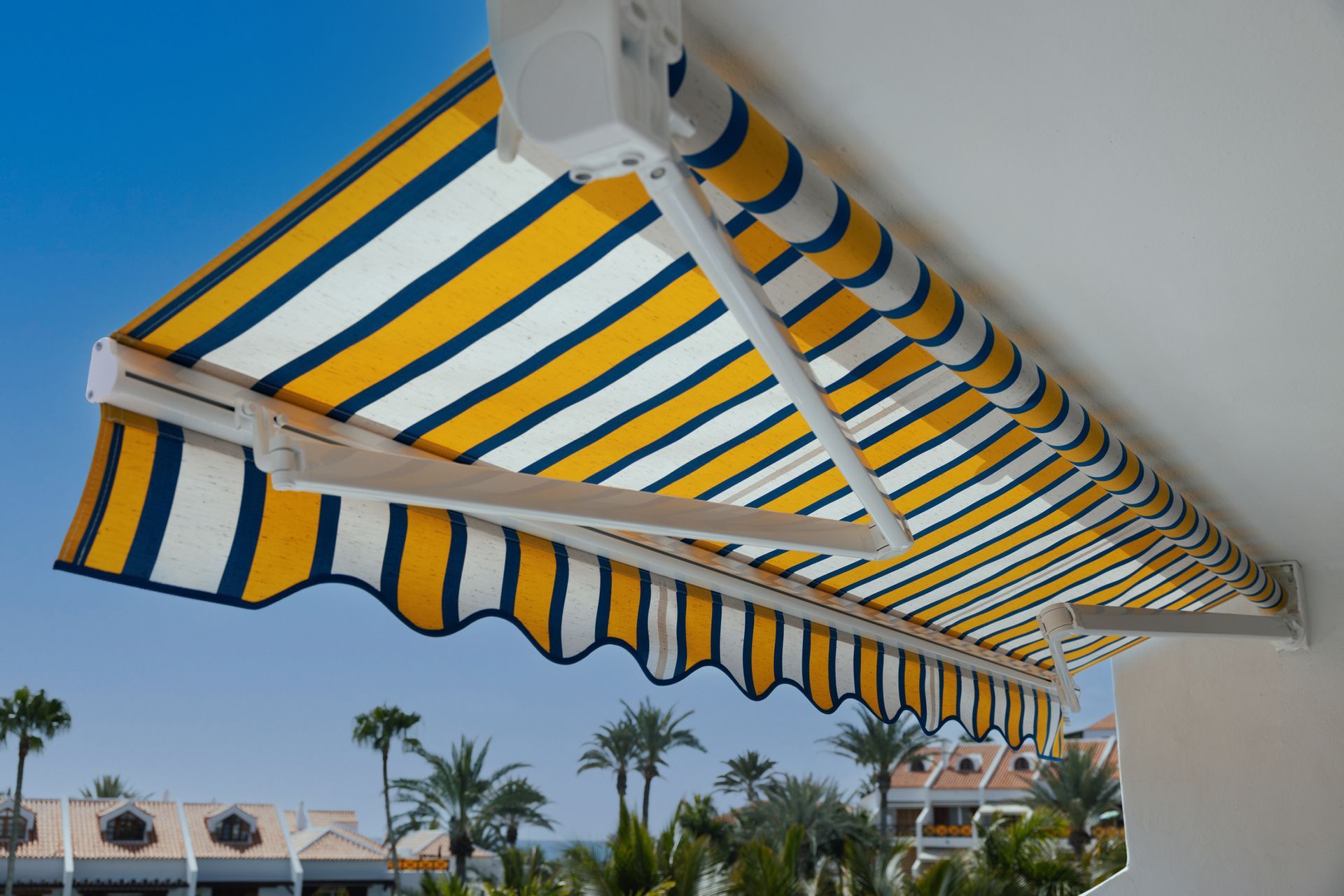 Blue and yellow striped awning extended over a balcony with palm trees view.