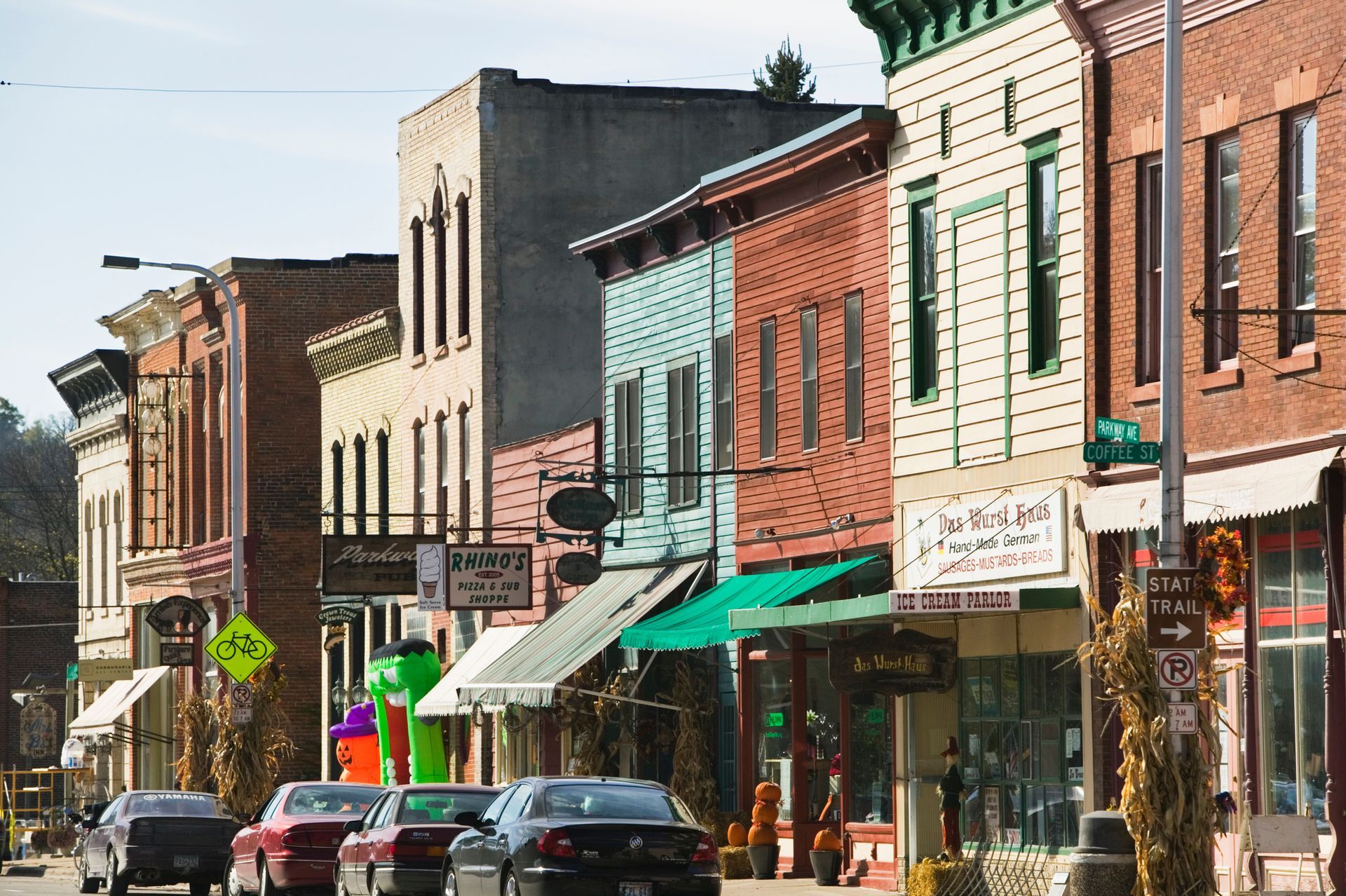 Row of colorful storefronts on a sunny street; cars parked, shops with awnings.