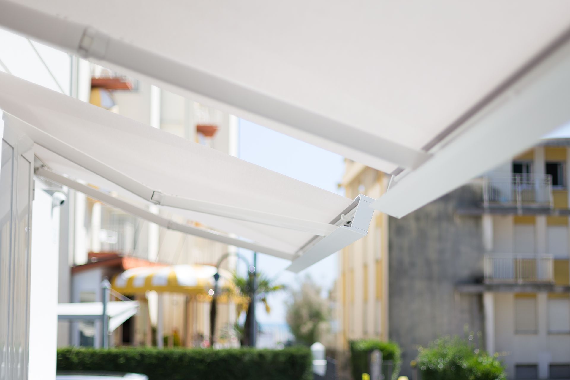 A white awning is covering a balcony with a building in the background - Freehold, NJ - Awning Design Inc