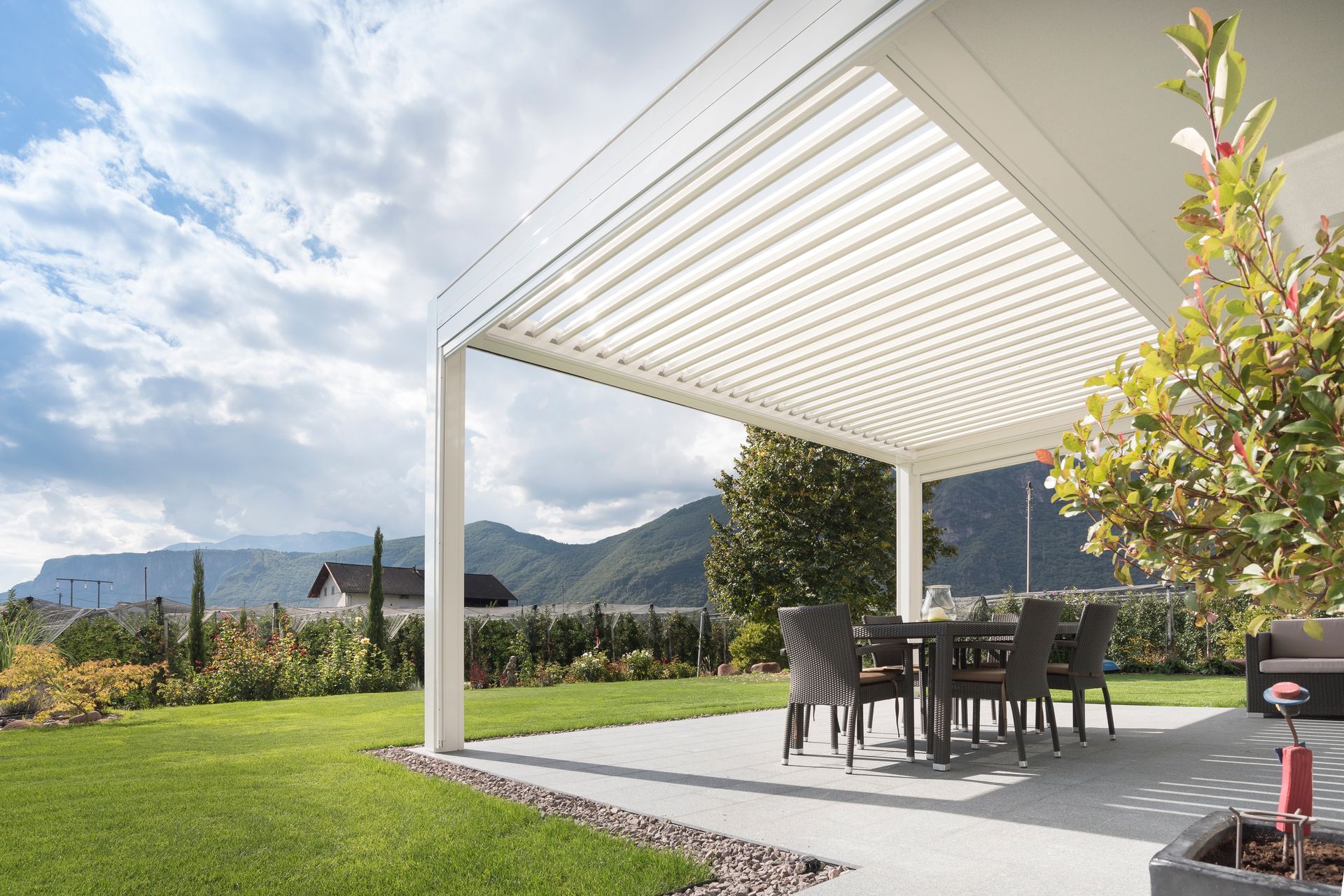 A patio with a table and chairs under a pergola with mountains in the background - Freehold, NJ - Awning Design Inc