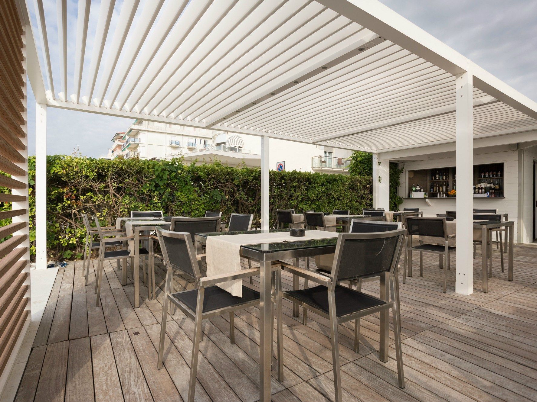 A wooden deck with tables and chairs under a white pergola - Freehold, NJ - Awning Design Inc